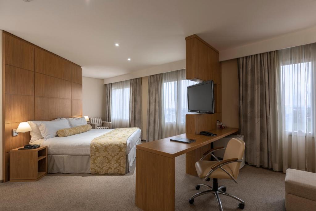 a hotel room with a bed and a desk and a tv at Monreale Plus São José dos Campos in São José dos Campos
