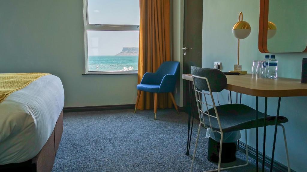 a hotel room with a bed and a desk and chairs at Marine Hotel Ballycastle in Ballycastle