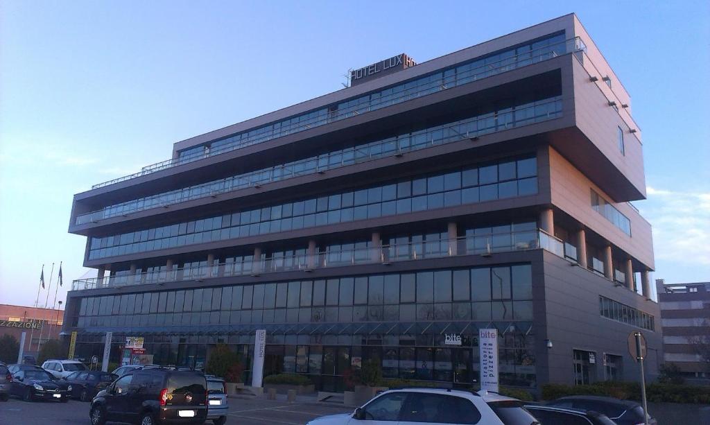 duży budynek z samochodami zaparkowanymi na parkingu w obiekcie Hotel Lux w mieście Modena