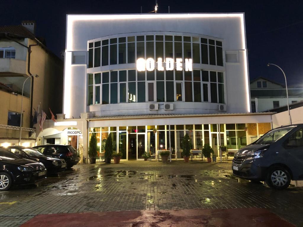 ein großes Gebäude mit Autos auf einem Parkplatz in der Unterkunft Golden BnB Hotel in Pristina