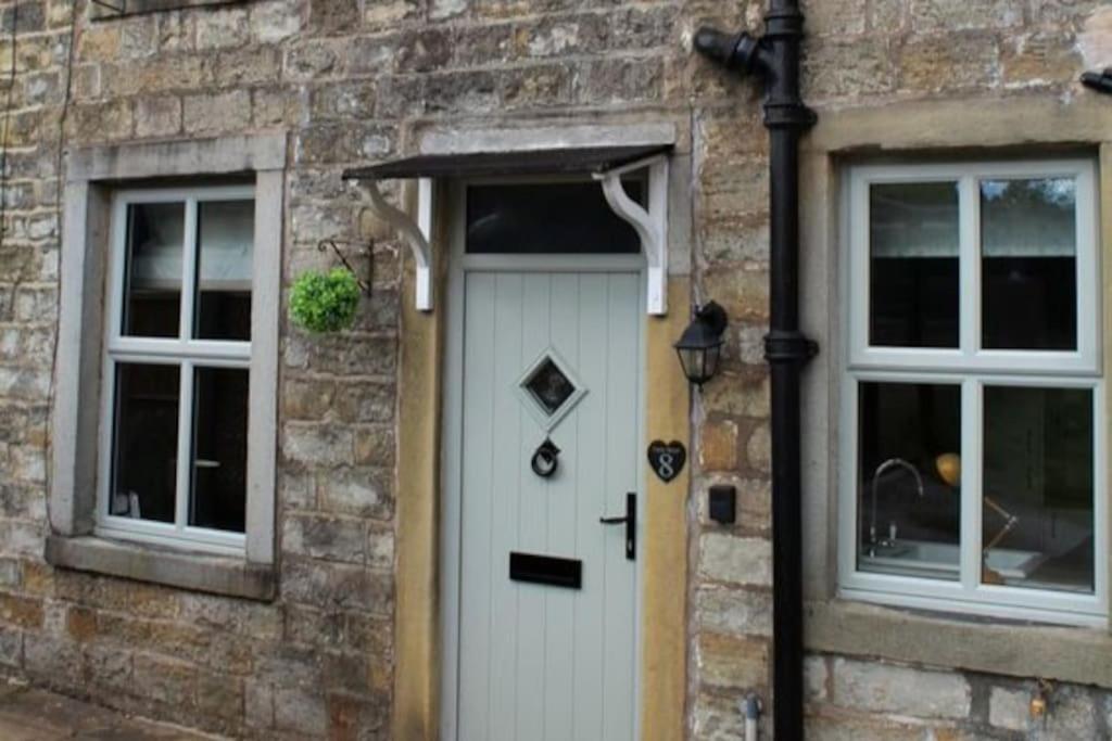 a white door on a brick building with two windows at Caterpillar Cottage, tucked away in Kelbrook in Kelbrook