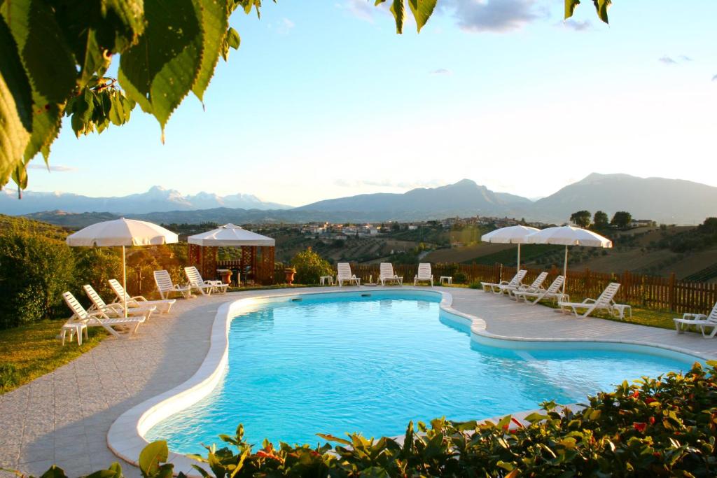 una piscina con sillas, sombrillas y montañas de fondo en Agriturismo Villa Fiore, en Torano Nuovo