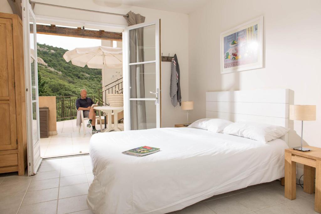 - une chambre avec un lit blanc et une personne assise sur un balcon dans l'établissement Villages Clubs du Soleil - LE REVERDI, à Grimaud