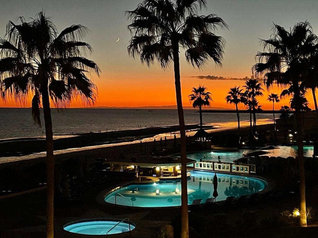 una piscina resort con palmeras y el océano al atardecer en Sonoran Sea Resort BEACHFRONT Condo E203 en Puerto Peñasco