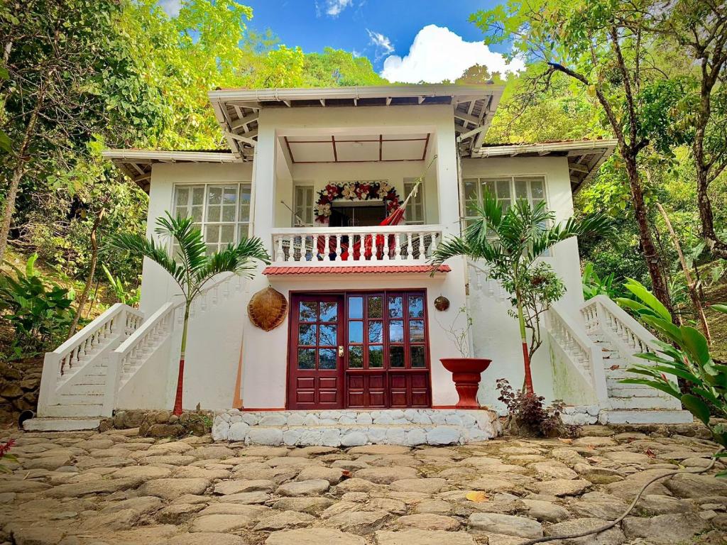 a white house with a red door and a balcony at Casa Hotel Arcadia Minca in Minca