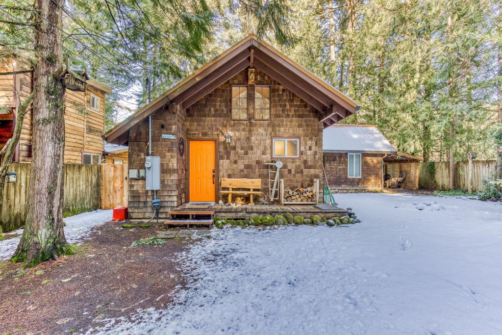 una cabaña de madera con una puerta naranja en la nieve en Cedar Cabin, en Welches