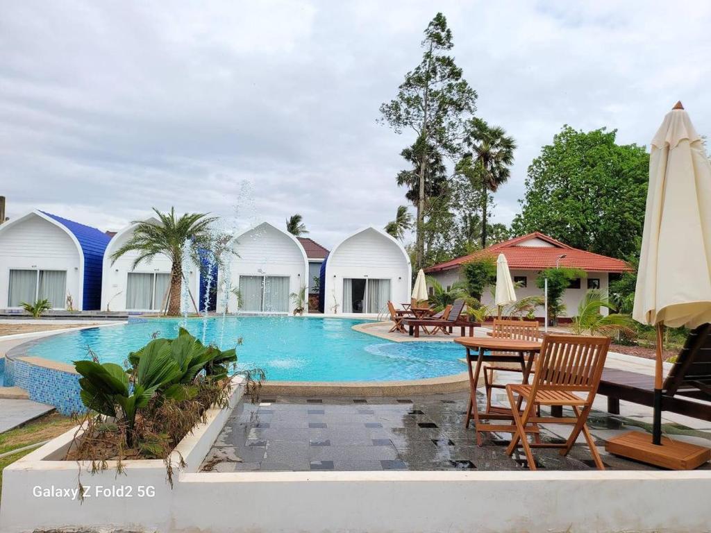 una piscina con mesa, sillas y sombrillas en Kampheak Roath Bungalows en Kampot