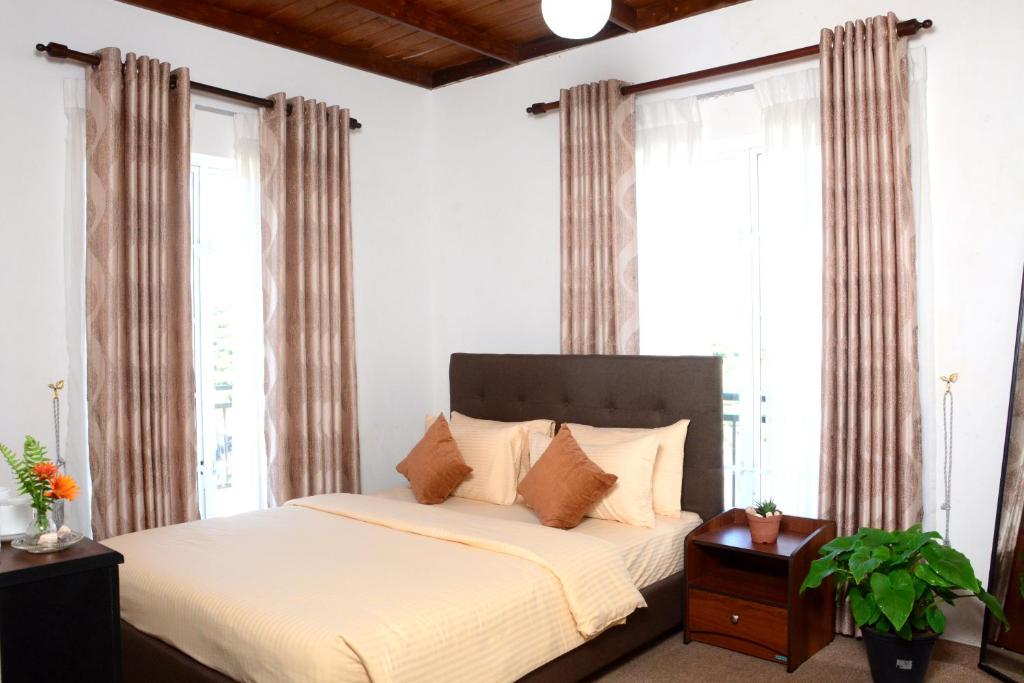 a bedroom with a bed with white sheets and windows at The Fern Inn in Nuwara Eliya