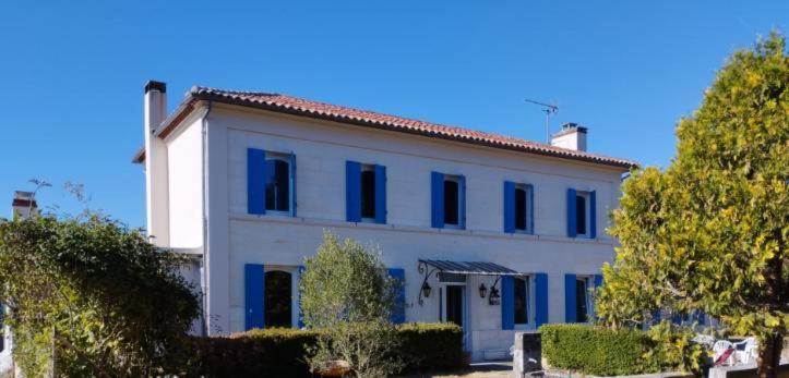 a large white building with blue windows and trees at La Coraillaise in Saint-Aigulin