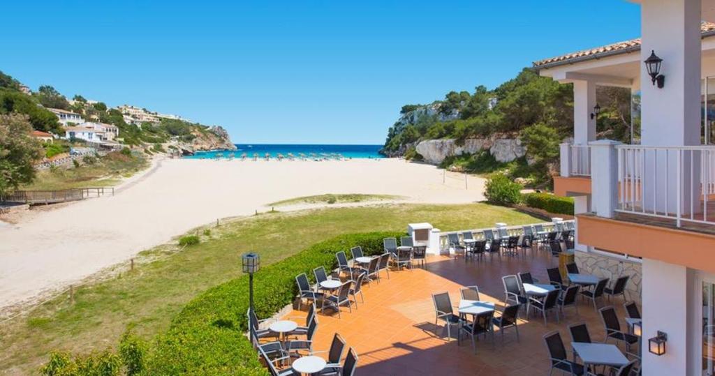a balcony with tables and chairs and a beach at FlipFlop Cala Romántica in Cala Romàntica
