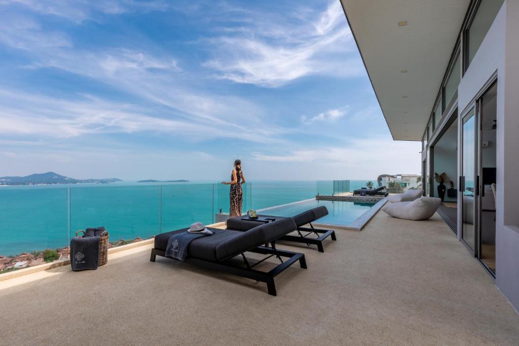 a woman standing on a balcony with a view of the ocean at Villa Anushka - Modern luxury villa with picture-perfect sea views in Koh Samui 