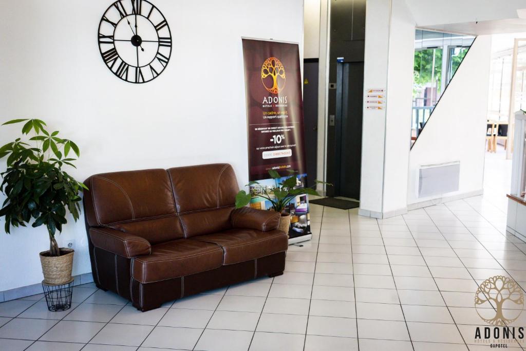 un fauteuil en cuir brun dans le hall avec une horloge dans l'établissement Adonis Gapotel, à Gap