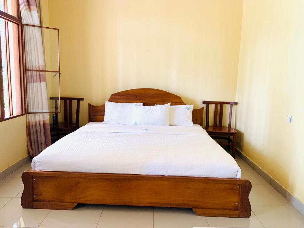 - une chambre dotée d'un lit en bois avec des draps et des oreillers blancs dans l'établissement EAR KEN BARHAM GUESTHOUSE, à Rwumba