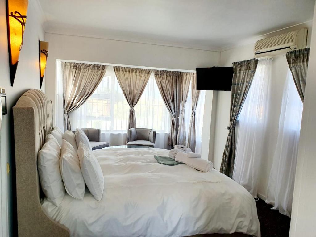 a bedroom with a large white bed with windows at La Grace Executive Guesthouse in Amsterdamhoek