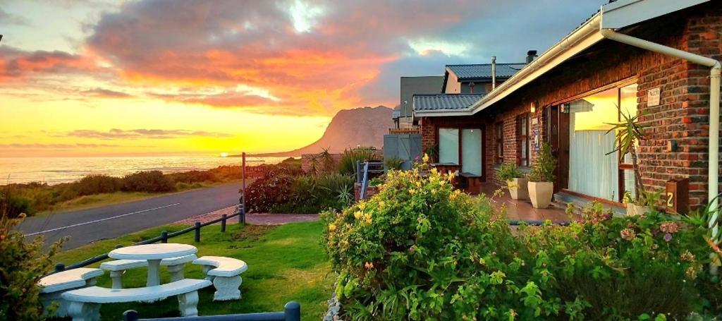 a house with a picnic table in front of a sunset at La Mer Seafront Selfcatering Accommodation Kleinmond in Kleinmond