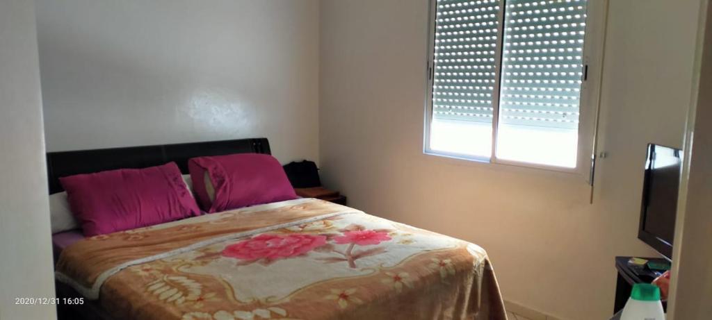 Un dormitorio con una cama con almohadas rosas y una ventana en APPARTEMENT ARRAJA, en Casablanca