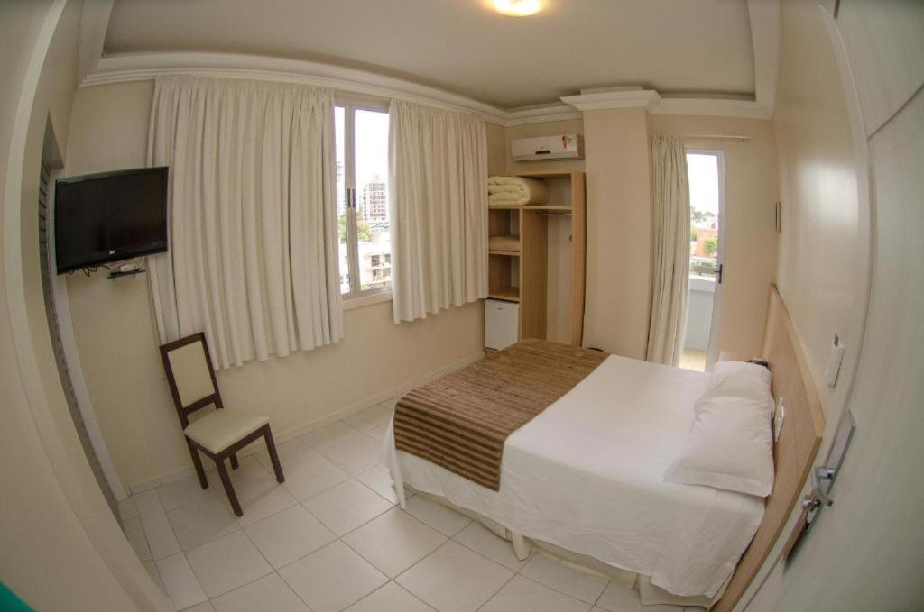 1 dormitorio con cama, silla y ventana en Hotel Desbravador, en Chapecó