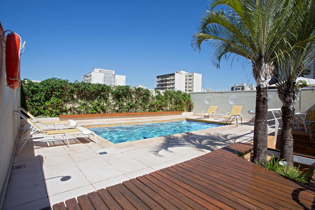 una piscina con sillas y palmeras en un edificio en Black Stream Hotel, en Ribeirão Preto