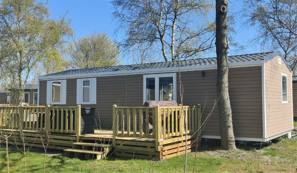 a tiny house with a porch and a deck at Bj Chalets - De Rug 3 - Vakantiepark Lauwersoog - Luxe kindvriendelijke chalet MET vaatwasser en inloopkast! Vroege incheck! in Lauwersoog