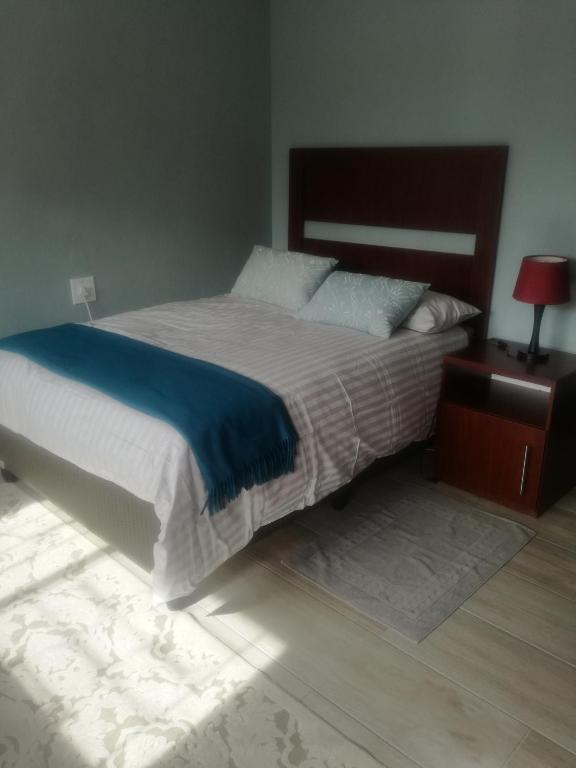 a bedroom with a large bed with a blue blanket and a table at Maseru Home with a View in Maseru