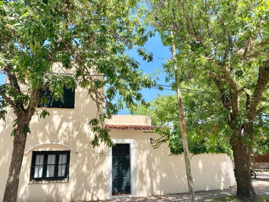 una casa blanca con árboles delante de ella en Hermosa casa céntrica, menos en euro usd en San Antonio de Areco
