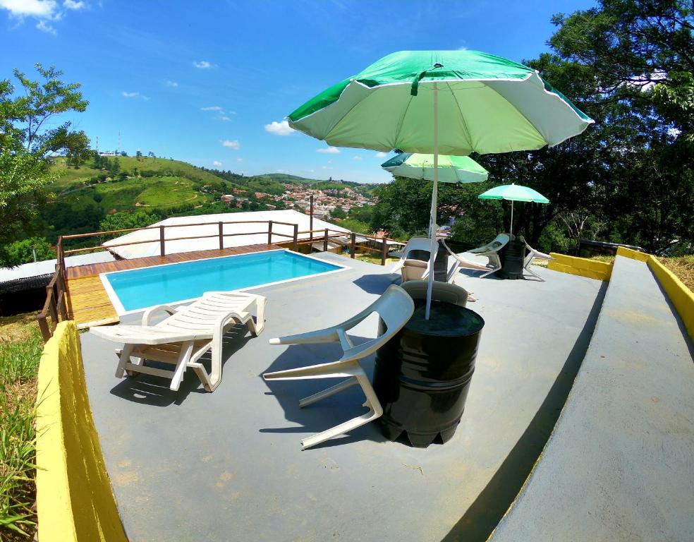 a pool with a green umbrella and chairs and a table at Pousada Solar da Montanha in Pedreira
