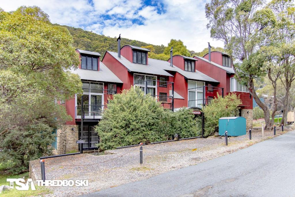 a red house with a fence in front of a street at Ironmongie 1 JackFrost in Thredbo
