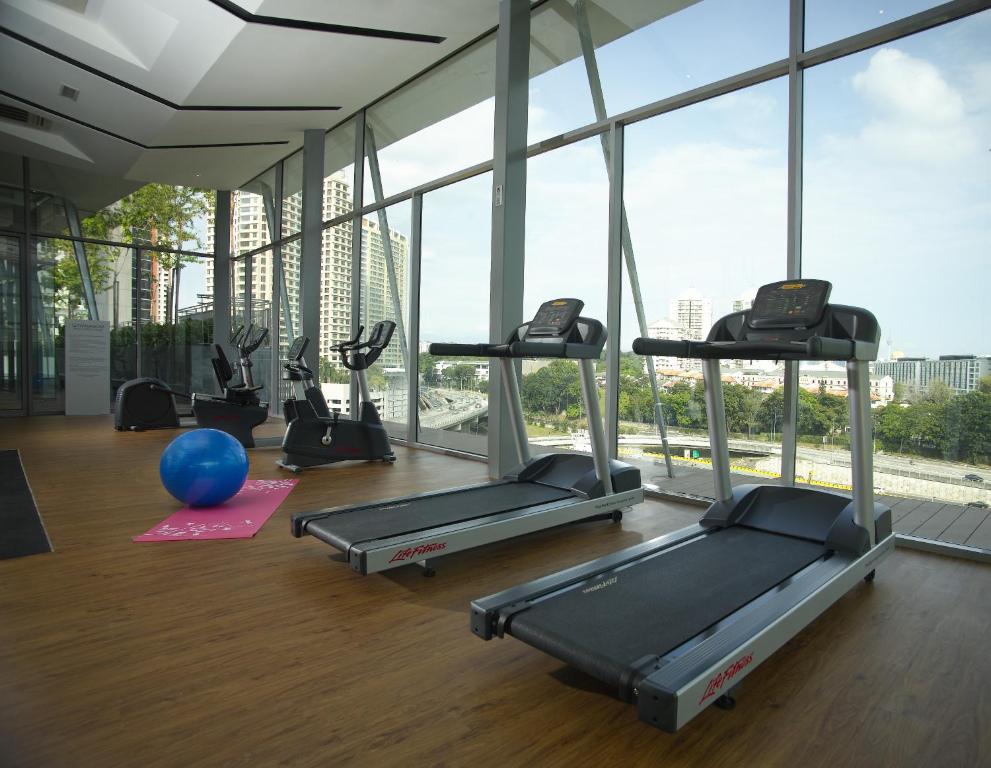 A glass-walled fitness room with two treadmills, cardio machines, and an urban view.