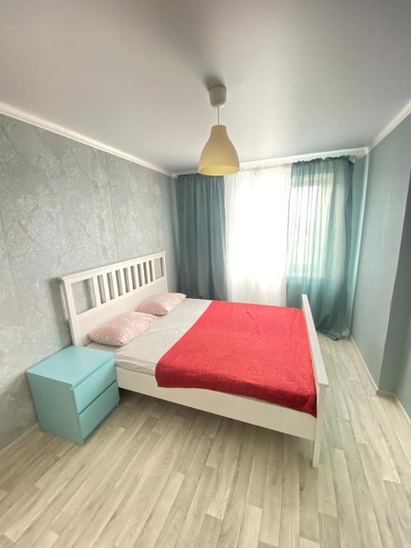 um quarto com uma cama com um cobertor vermelho e uma janela em 2-х комнатная квартира напротив аквапарка em Aqtöbe