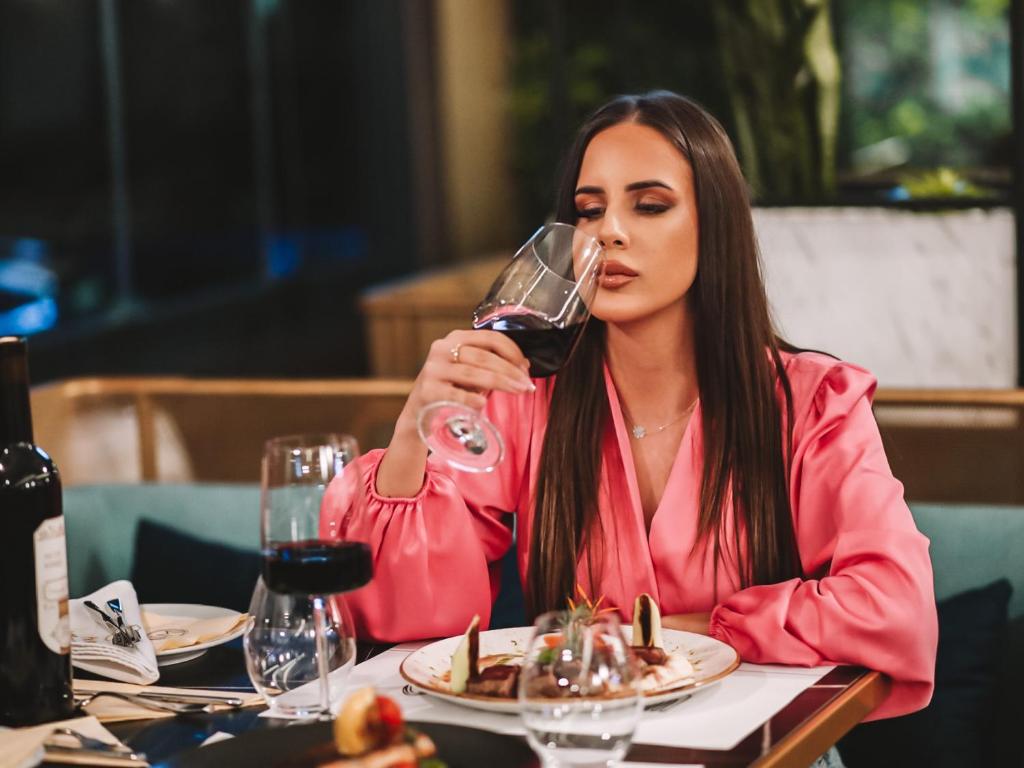 a woman sitting at a table drinking a glass of wine at Hotel Millennium by Aycon in Budva