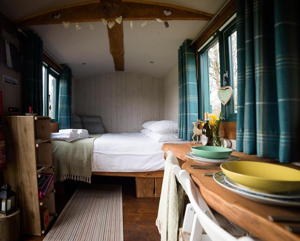 a bedroom with a bed and a wooden table with bowls on it at Shire the Shepherd's Hut at Pentref Luxury Camping in Penuwch