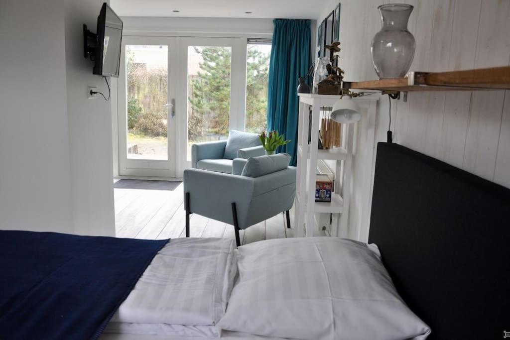 a bedroom with a bed and a chair and a window at Anna, strandhuisje dichtbij zee & strand! in Callantsoog