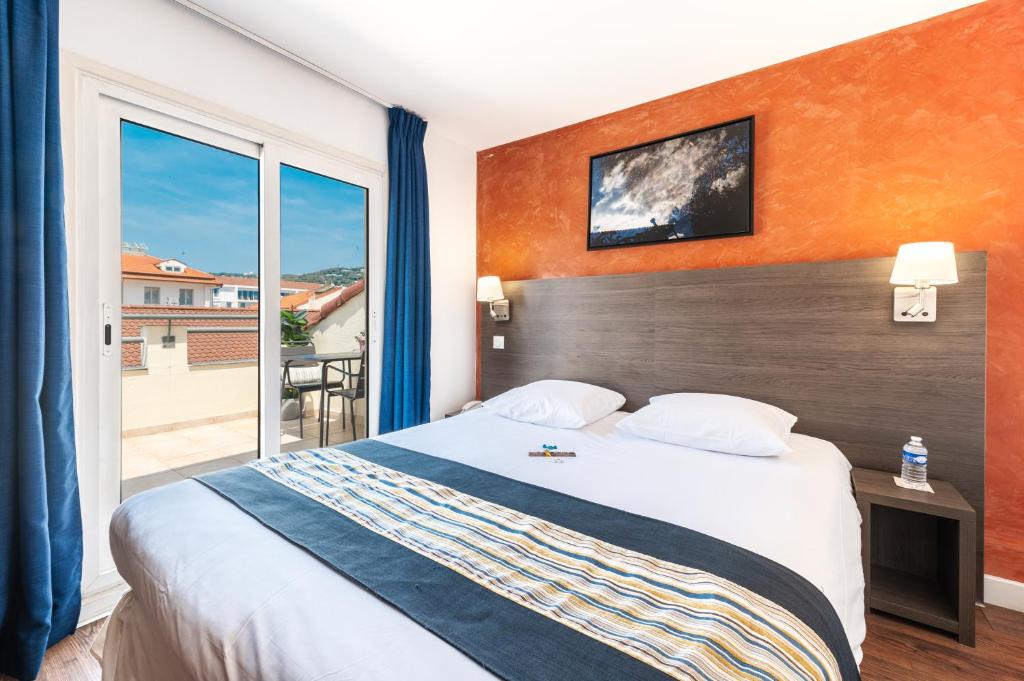 a hotel room with a bed and a large window at Hôtel Hoche in Cannes