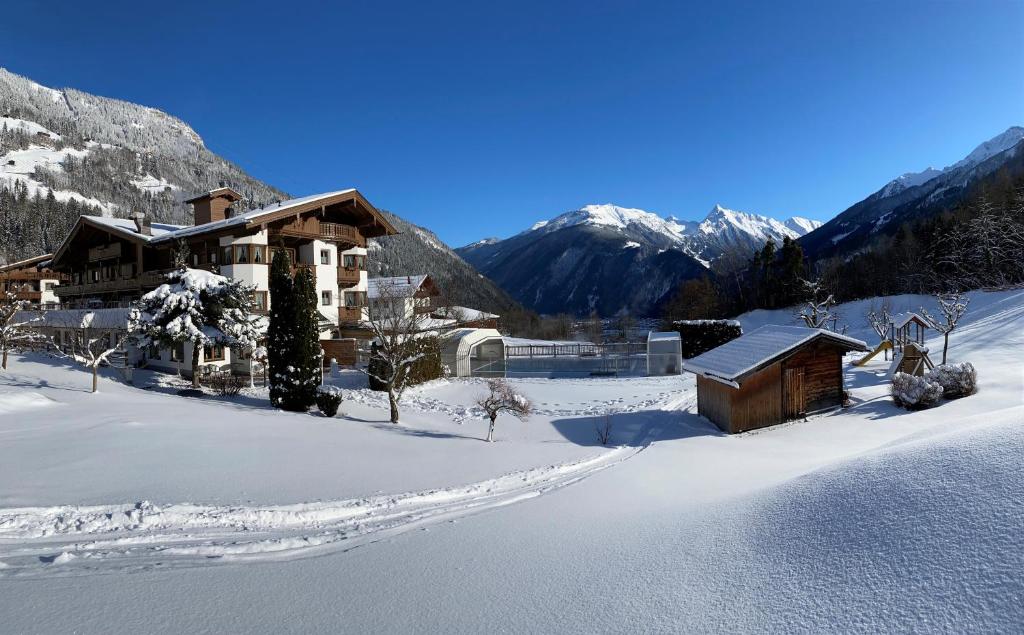 a house in the snow with mountains in the background at Olympia-Relax-Hotel Leonhard Stock in Finkenberg