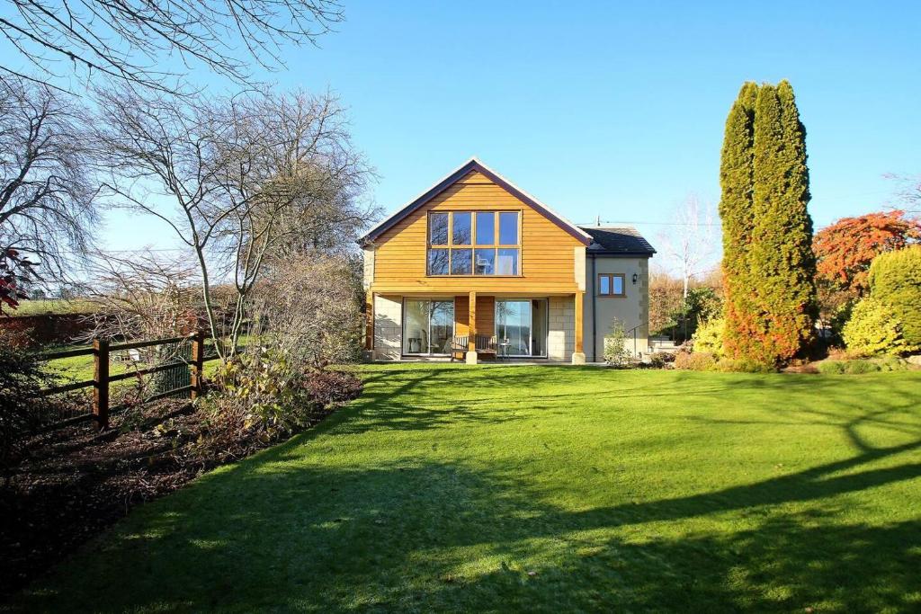 a yellow house on a green lawn with a fence at Dove Lodge in Painswick in Stroud