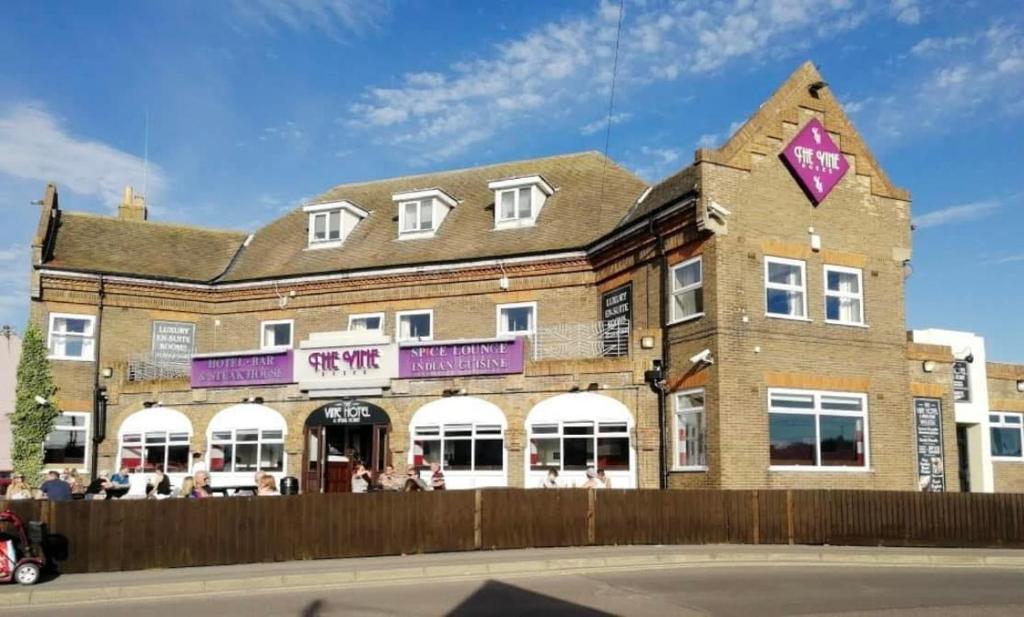 een groot bakstenen gebouw met een roze bord erop bij The Vine Hotel Chapel st Leonards in Skegness