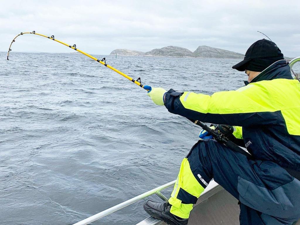 a man in a yellow jacket holding a fishing pole in the water at Holiday home Nuvsvåg 