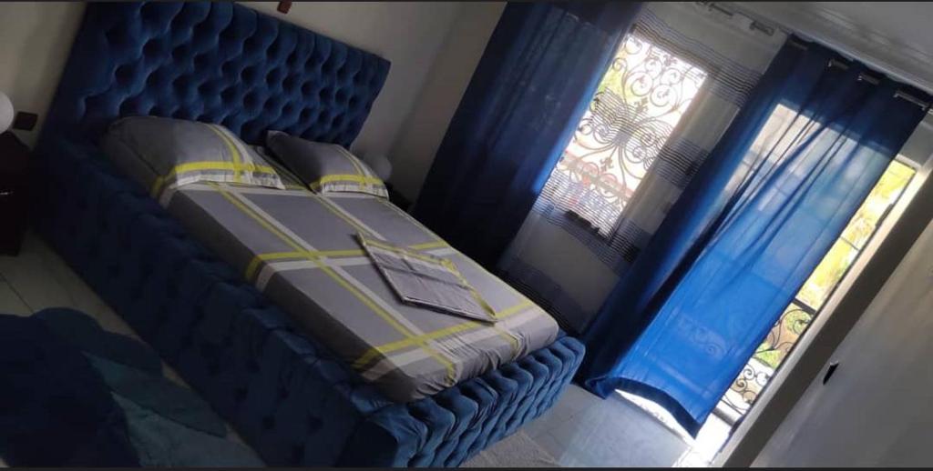 a bedroom with a bed and two windows with blue curtains at Studios-Appartements meublés Makepé BM in Douala