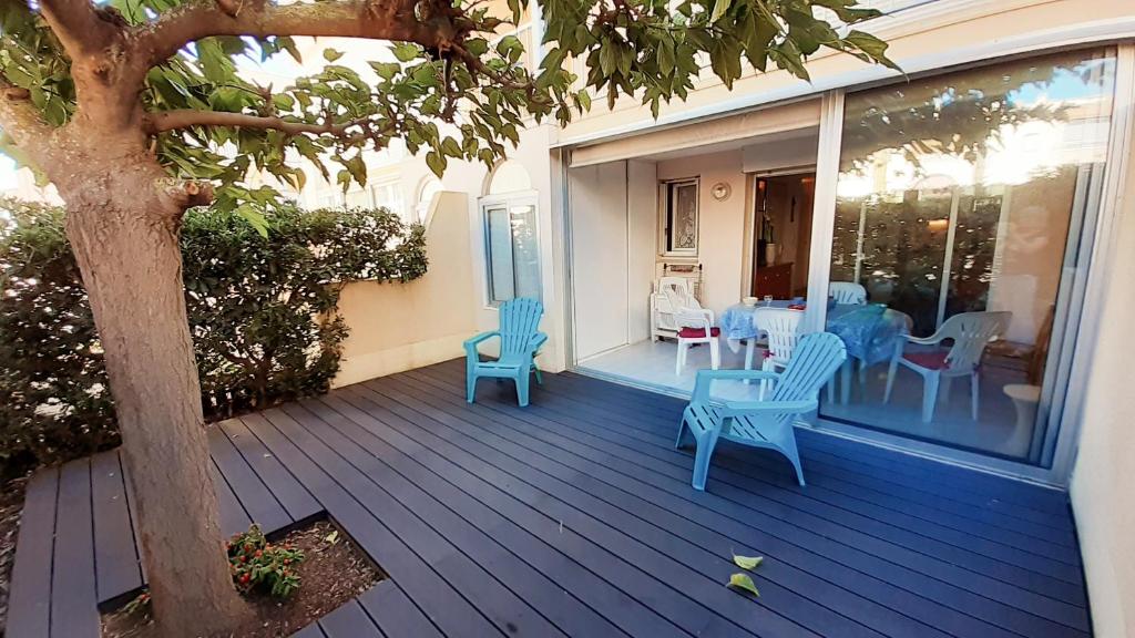 une véranda avec des chaises bleues, une table et un arbre dans l'établissement ARCHIPEL III Joli T2 piscine proche plage Richelieu Cap d'Agde, au Cap d'Agde