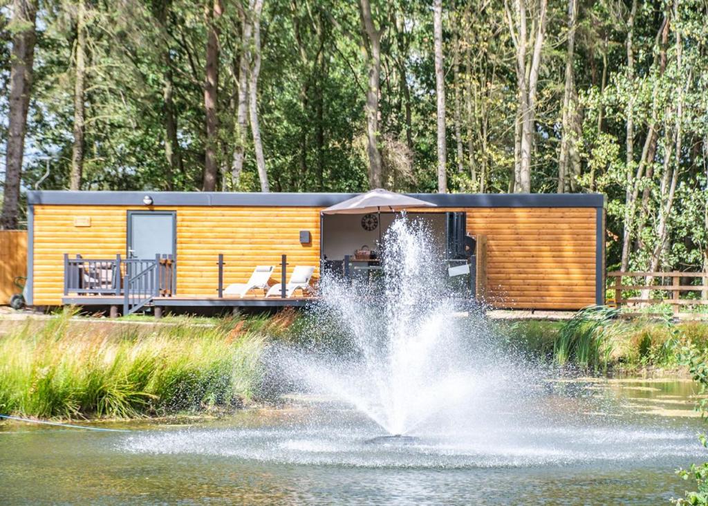 a luxurious tiny house with a fountain in front of a pond at Woodland Lakes Boutique Lodges 