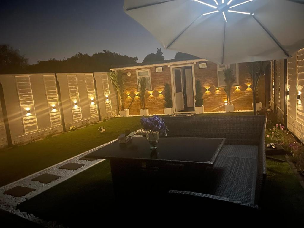 eine Terrasse mit einem Tisch und einem Sonnenschirm in der Nacht in der Unterkunft North Avenue, Guest House, Heathrow Airport-Free Parking in Hayes