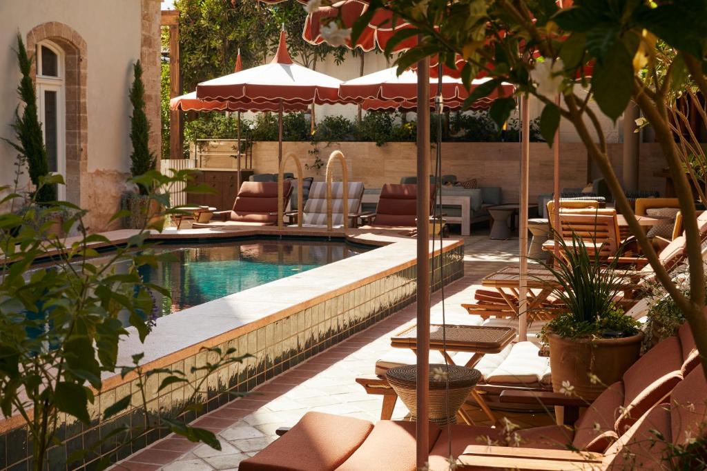 a swimming pool with chairs and umbrellas next to a patio at Soho House Tel Aviv in Tel Aviv
