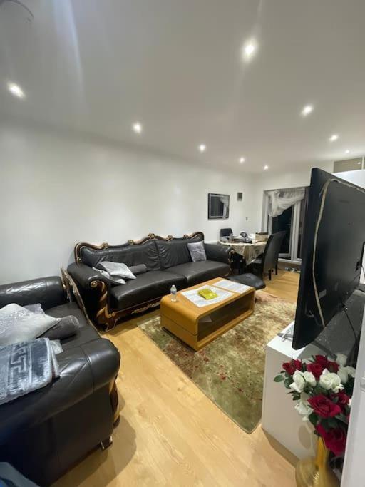 sala de estar con sofá negro y TV en 2 Bedroom House - West London, en Northolt