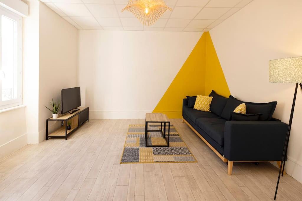 een woonkamer met een zwarte bank en een gele muur bij Le Cosy C - T2 Tout Équipé - Centre-Ville Gare in Montluçon