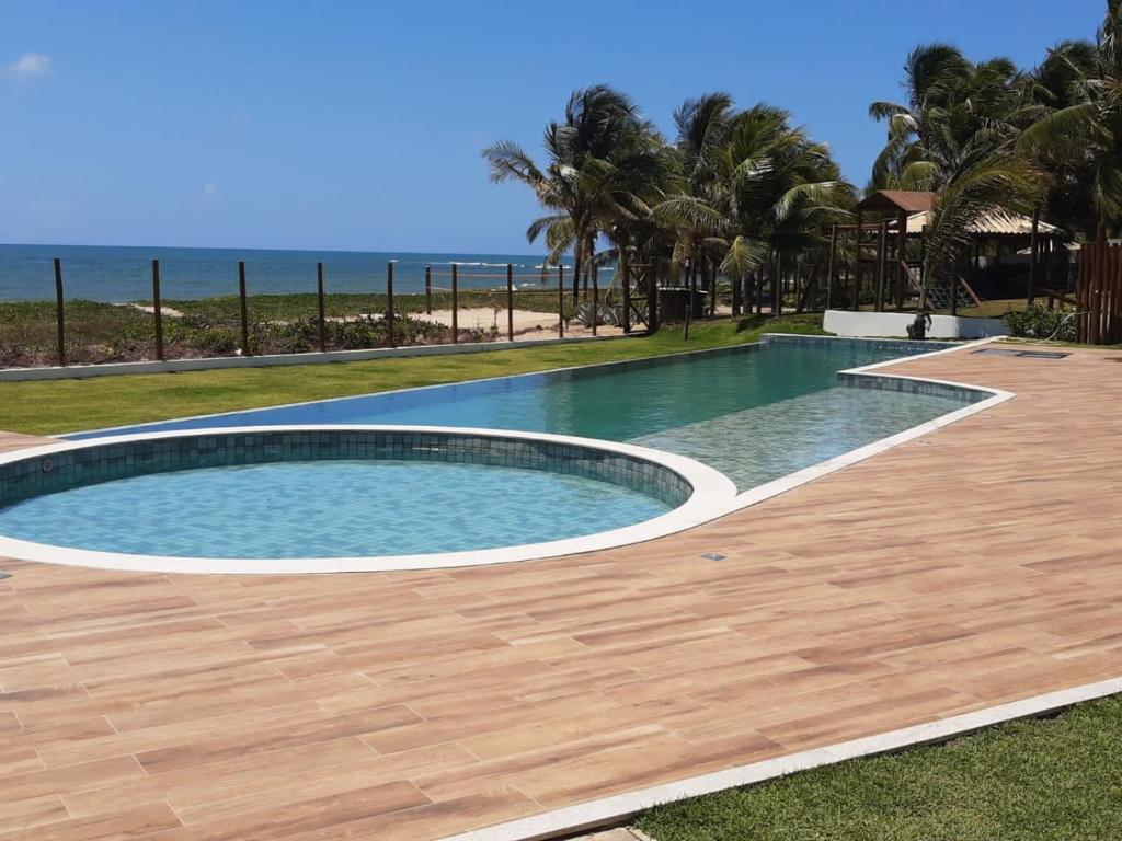 a swimming pool with a wooden deck and the beach at Itacimirim Beira Mar in Itacimirim