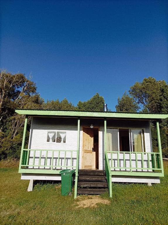 a small white house with a porch and a green trash can at Cabañas Aulen Chepu Chiloe in Ancud