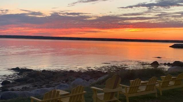 una puesta de sol sobre un cuerpo de agua con dos sillas en Whispering Waves Cottages, en Shelburne