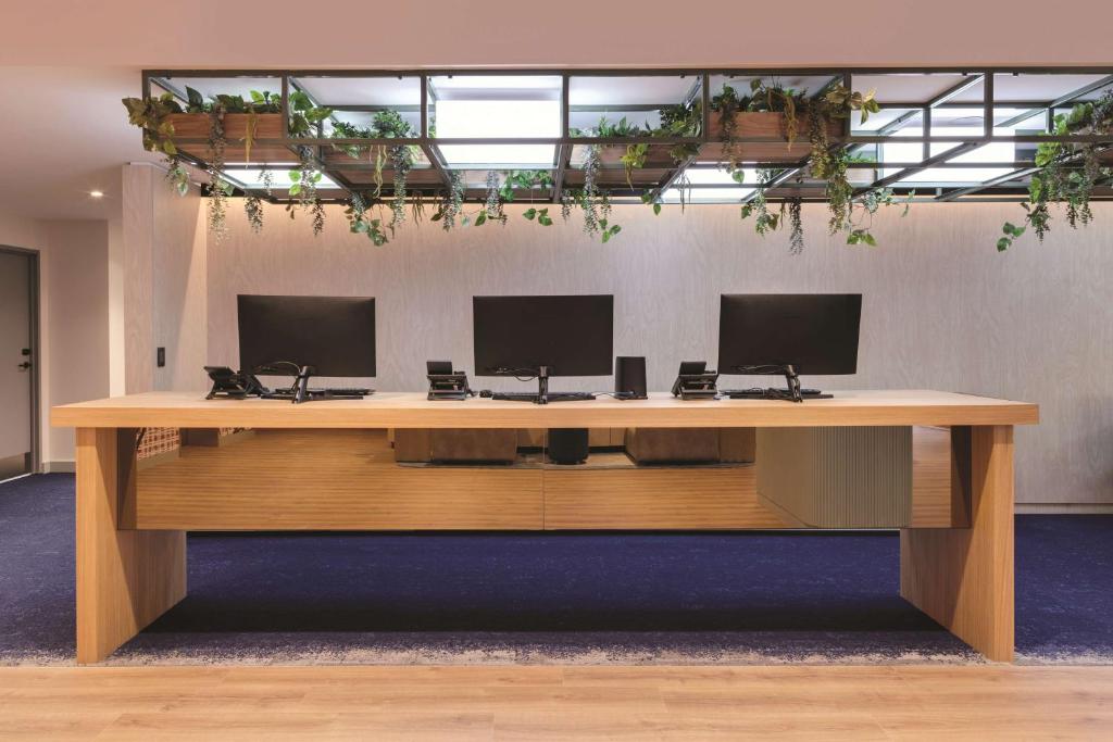 a wooden desk with three monitors on top of it at Travelodge Hotel Hurstville Sydney in Sydney