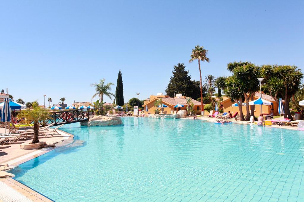 a large swimming pool in a resort with palm trees at Makronisos Village in Ayia Napa
