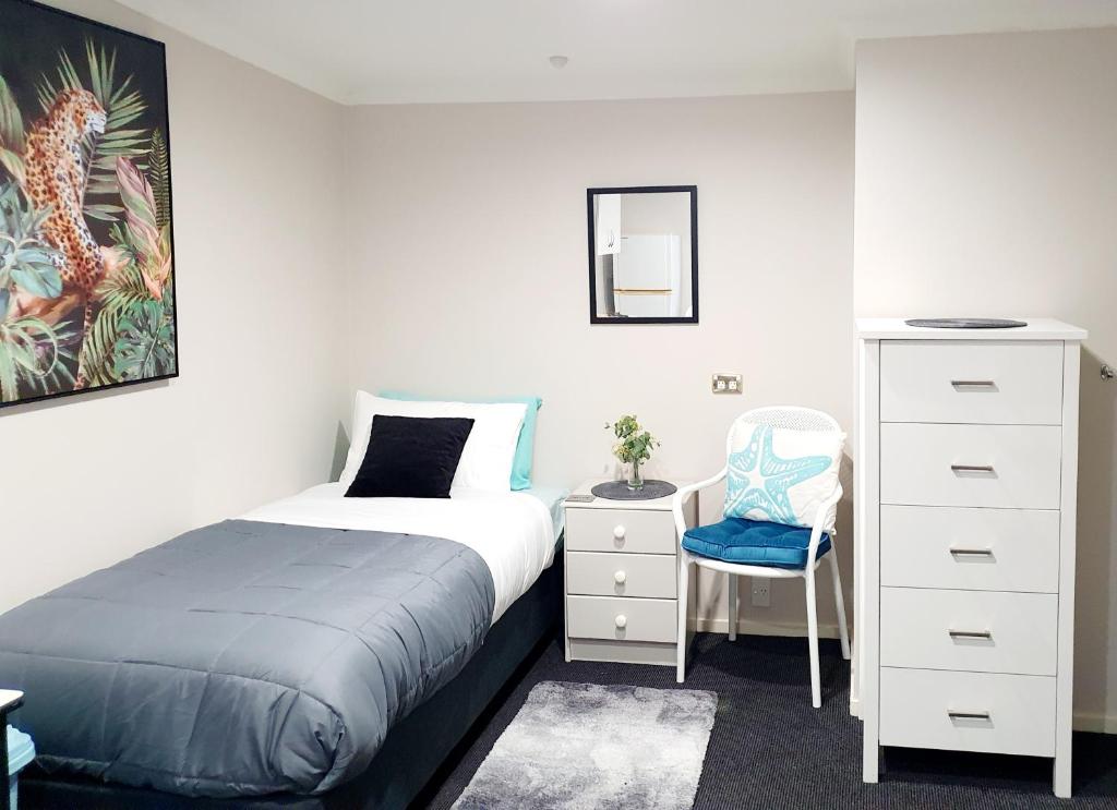 a bedroom with a bed and a dresser and a chair at Extended Stay City Hostel in Dunedin